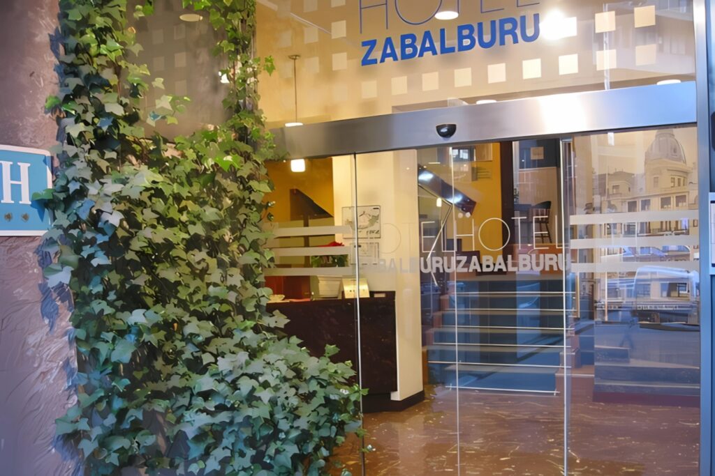 Entrada principal del Hotel Photo Zabalburu con puertas de cristal automáticas y vegetación decorativa